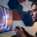 Jeune homme concentré jouant aux jeux vidéo avec un casque devant un écran incurvé lumineux.